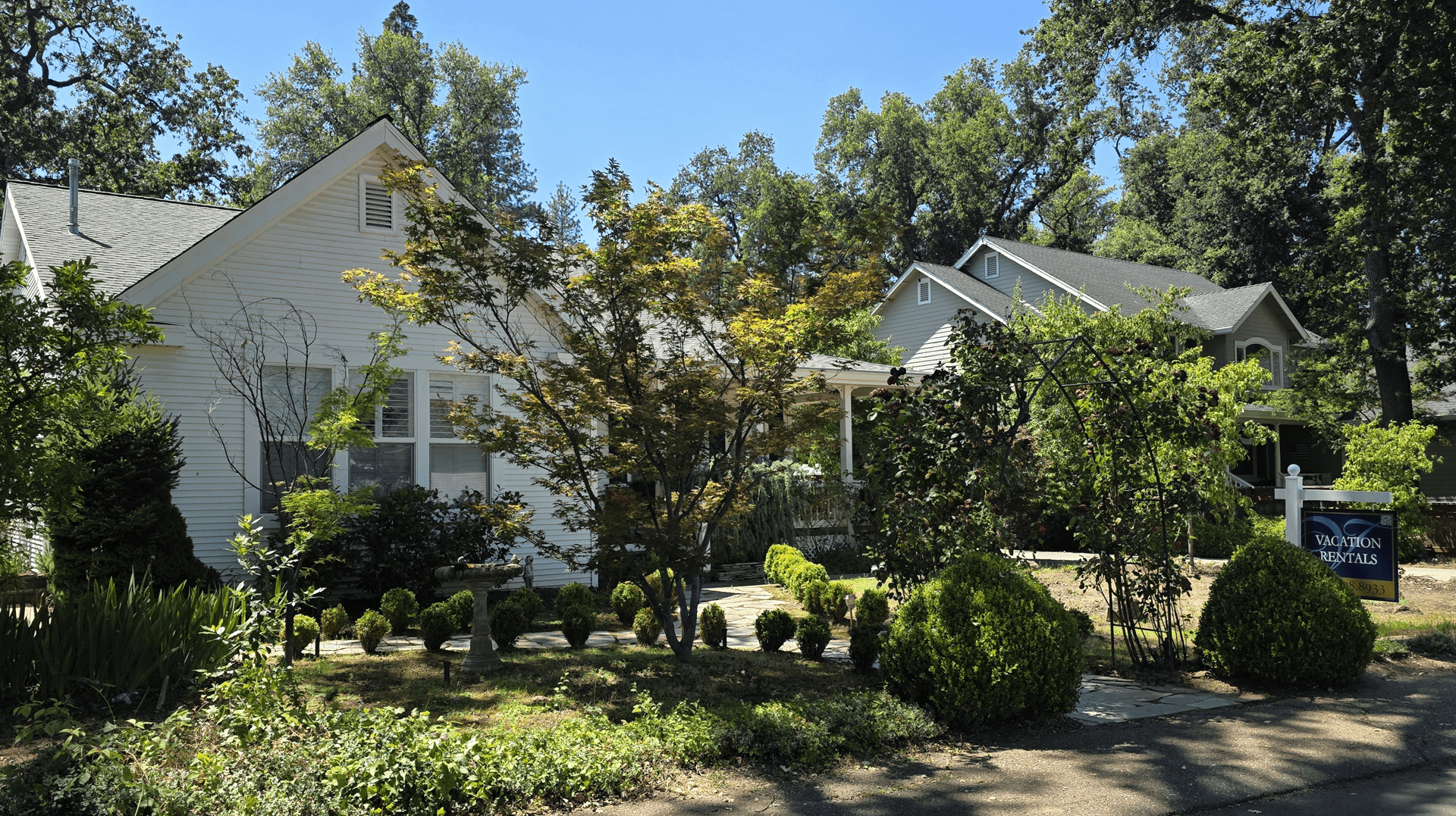 A charming house surrounded by lush greenery and neatly trimmed shrubs on a sunny day.